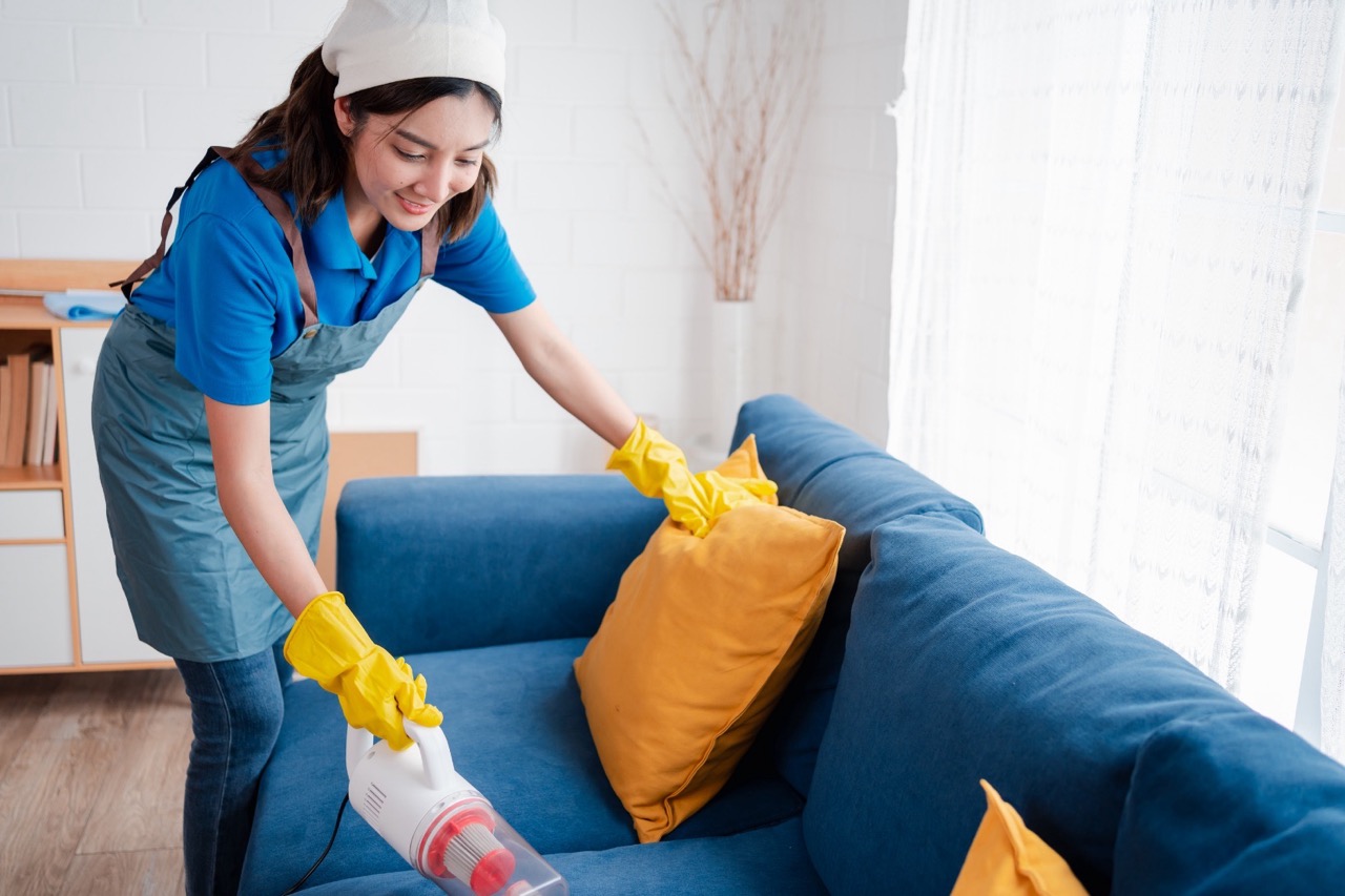 Professional cleaner vacuuming and tidying sofa and living area